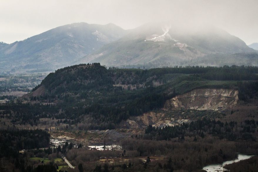A wide aerial view shows the extensive damage of the landslide after taking out a chunk of earth from the side of the hill facing the Stillaguamish River, and down into the State Route 530, on the left, between the cities of Arlington and Darrington, on Saturday, March 22, 2014. Search and rescue operations are underway for survivors. (AP Photo/ The Seattle Times, Marcus Yam )