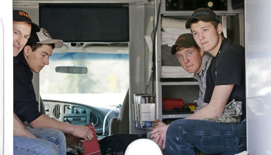 Volunteers wait in the back of a fire vehicle to be taken to the site of a deadly mudslide two days earlier to use chainsaws to help clear debris Monday, March 24, 2014. Officials said that there are currently 108 names of people who have been reported missing or are unaccounted for from the Saturday morning slide, but cautioned the figure would likely decline dramatically. Eight people are so far confirmed dead from the one-square mile slide that destroyed about 30 homes and critically injured several people. (AP Photo/Elaine Thompson)