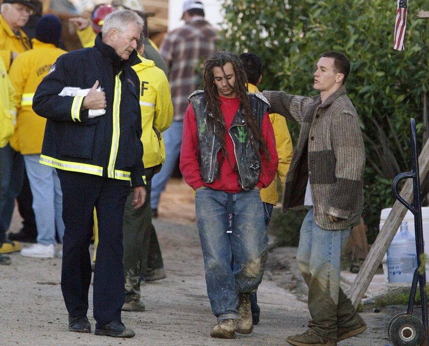 FILE - In this Tuesday, Jan. 11, 2005, file photo, an unidentified rescue worker left, consoles Jimmie Wallet, in leather jacket, whose wife and three children are missing in a mudslide, in La Conchita, Calif. The coastal Southern California town of La Conchita knows the sorrows that a major mudslide can unleash. In 2005, a wall of debris slammed down from a bluff soaked by winter storms, killing 10 people and damaging or destroying 36 homes. On Saturday, March 22, 2014, a mudslide hit Oso, Wash., where 14 people are confirmed dead, dozens more are thought to be unaccounted for or missing and about 30 homes are destroyed. (AP Photo/Damian Dovarganes, File)