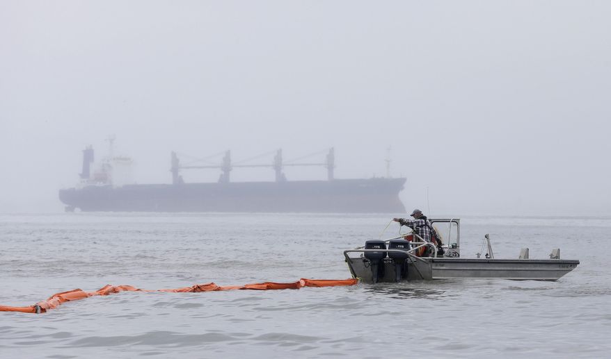 A boat drags an oil boom out into the water as a cargo ship sits in the ship waits to enter the ship channel along East Beach Monday, March 24, 2014, in Galveston, Texas. The booms are being placed along the coastline to help clean up the thousands of gallons of tar-like oil spilled into the major U.S. shipping channel after a barge ran into a ship Saturday. (AP Photo/Pat Sullivan)