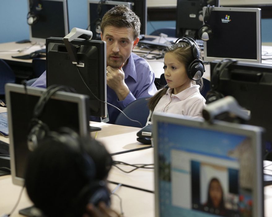 In this Feb. 26, 2014 photo, Bennett Elementary teacher Andy Clark helps student Stephanie Serratos, 9, with a student from Novi High School via Skype during a tutoring session in Detroit. The public school in Southwest Detroit helps students with one-on-one tutoring in the 4th and 5th grades via Skype with student volunteers at a suburban high school. (AP Photo/Carlos Osorio)