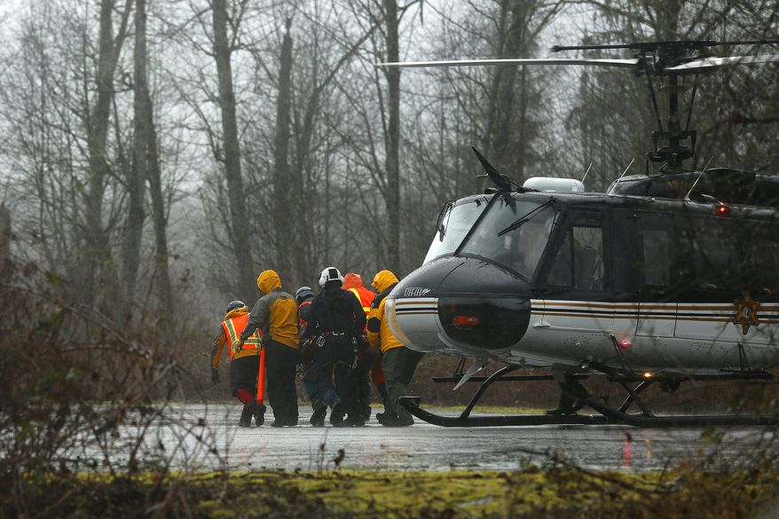A helicopter and waiting ground crew transfer a worker injured working on the mudslide into a waiting ambulance from a Snohomish County helicopter near Oso, Wash., Tuesday, March 25, 2014. A massive mudslide struck near Arlington, Wash., on Saturday, killing at least 14 people over the weekend and leaving scores more missing. (AP Photo/The Herald, Mark Mulligan)