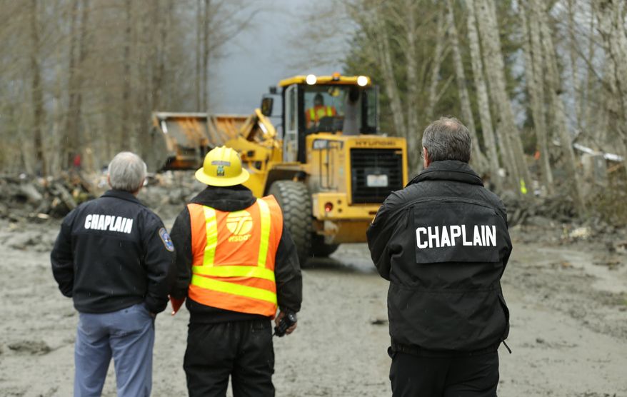 Washington State Patrol chaplains Joel Smith, left, and Mike Neil, right, watch as workers using heavy equipment work to clear debris, Tuesday, March 25, 2014, from Washington Highway 530 on the western edge of the massive mudslide that struck near Arlington, Wash. Saturday, killing at least 14 people and leaving dozens missing. (AP Photo/Ted S. Warren, Pool)