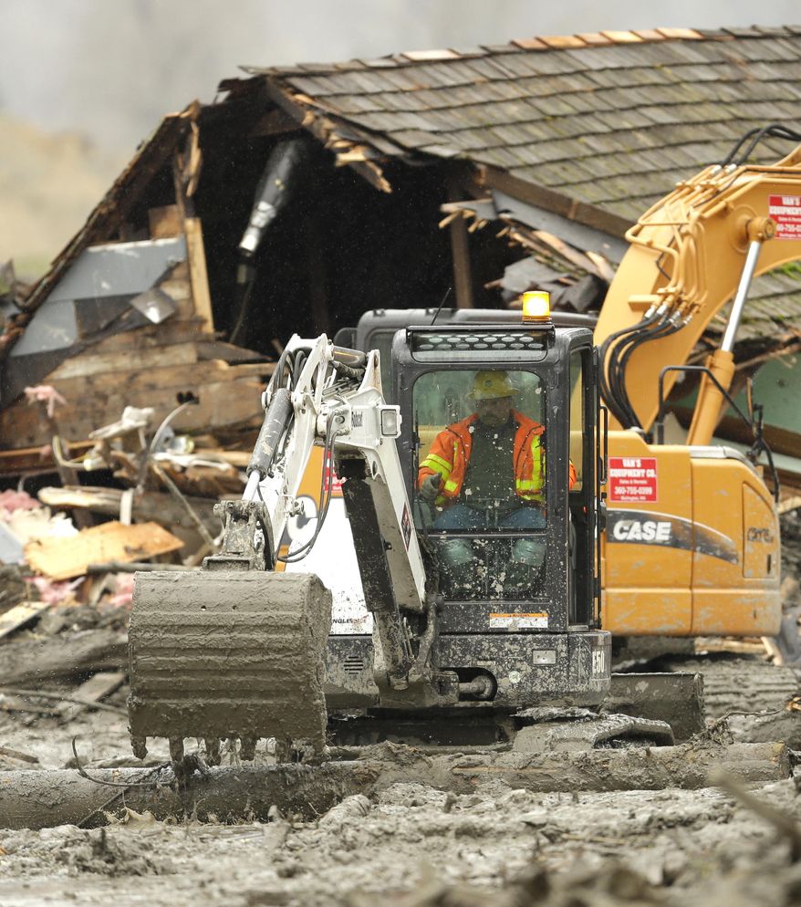 Workers using heavy equipment work to clear debris Tuesday, March 25, 2014, near a destroyed house that came to rest on Washington Highway 530 on the western edge of the  massive mudslide that struck near Arlington, Wash., Saturday, killing at least 14 people and leaving dozens missing. (AP Photo/Ted S. Warren, Pool)