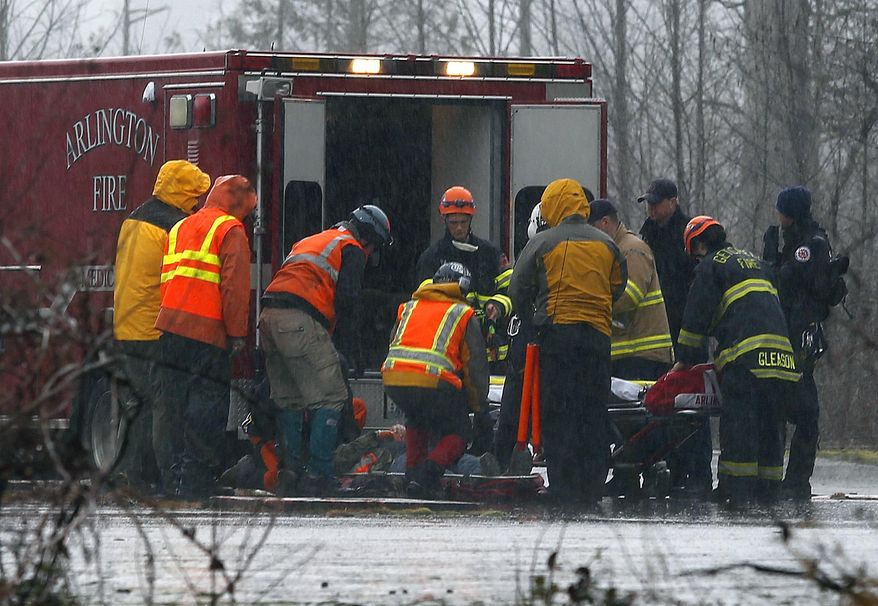 A helicopter and waiting ground crew transfer a worker injured working on the mudslide into a waiting ambulance from a Snohomish County helicopter, Tuesday, March 25, 2014, near Oso, Wash. A massive mudslide struck near Arlington, Wash., on Saturday, killing at least 14 people over the weekend and leaving scores more missing. (AP Photo/The Herald, Mark Mulligan)
