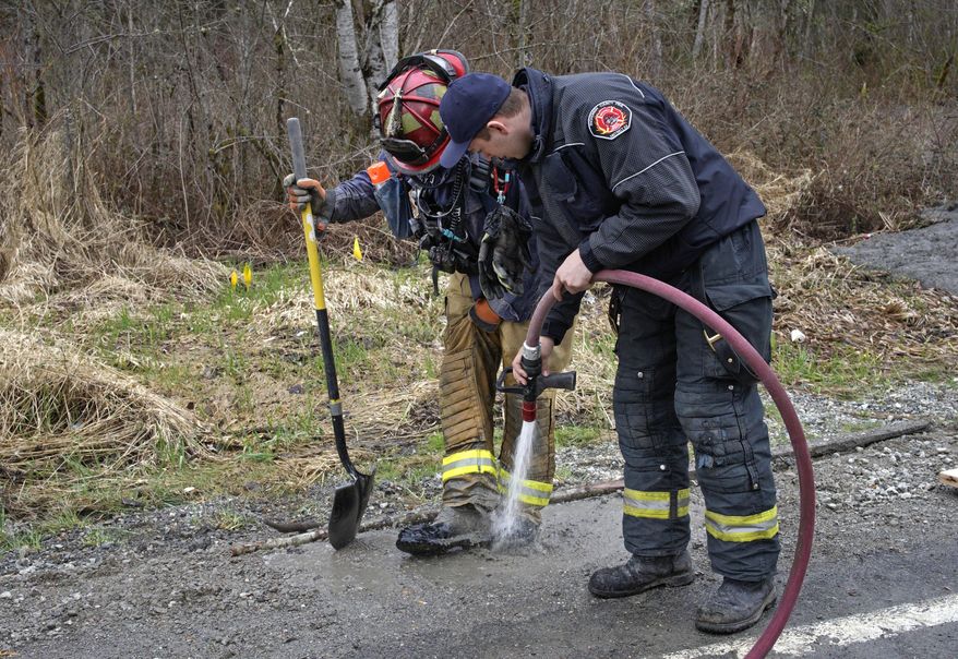 A searcher is hosed-down after working at the scene of a deadly mudslide that covers the road, Wednesday, March 26, 2014, in Oso, Wash. Sixteen bodies have been recovered, but authorities believe at least 24 people were killed. And scores of others are still unaccounted for, although many of those names were believed to be duplicates or people who escaped safely. (AP Photo/Rick Wilking, Pool)