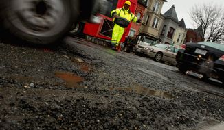 A worker directs traffic through potholes that mark the surface along Florida Ave. in Northwest. (Andrew Harnik/The Washington Times)
