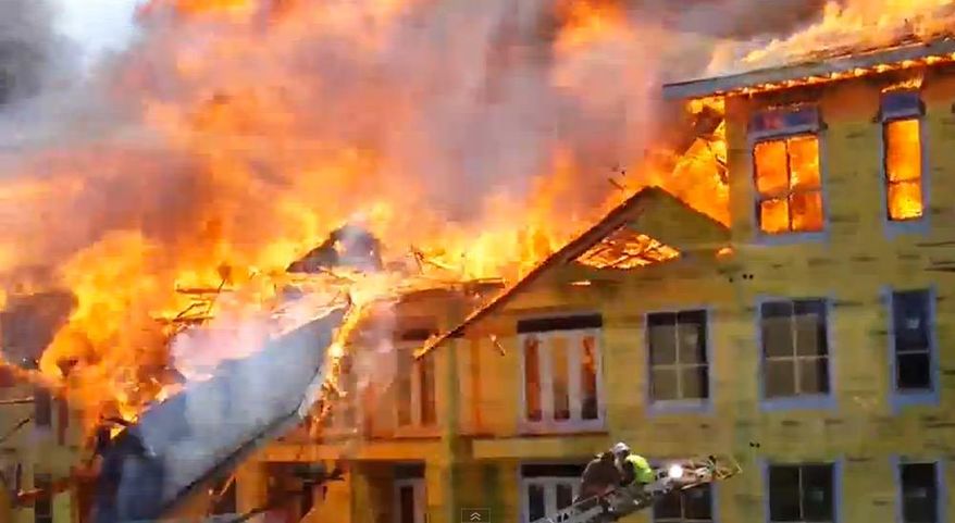 In this image taken from video provided by Karen Jones, a burning section of wall collapses moments after a worker was rescued from a balcony by firefighters battling a five-alarm fire at a construction site Tuesday, March 25, 2014, in Houston. The cellphone video, shot by Karen Jones from her nearby office, shows the dramatic rescue of the worker from the burning apartment complex that was under construction. (AP Photo/Karen Jones) NO SALES