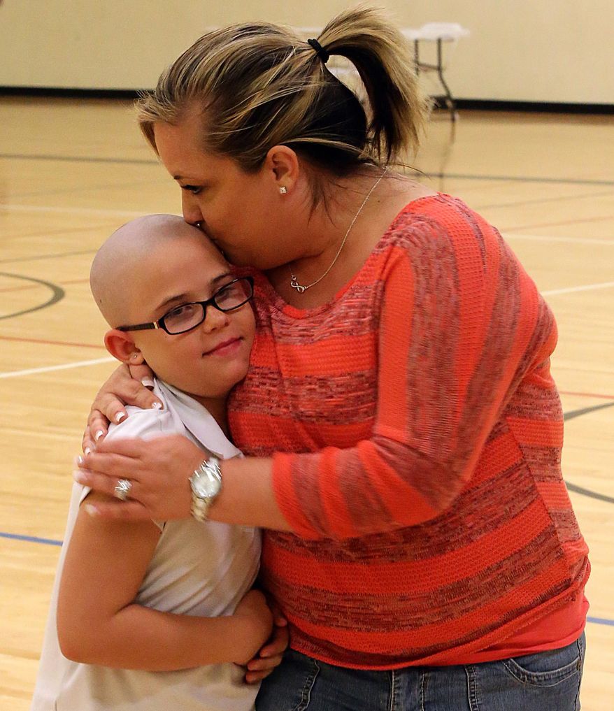 In this photo taken on Tuesday, March 25, 2014, Jamie Renfro hugs and kisses her daughter Kamryn, 9, after meeting with the Caprock Academy board of directors in the gym at the school in Grand Junction, Colo. The board of directors of the charter school voted Tuesday to let Kamryn remain at school, after officials had earlier barred her, saying she violated the dress code by shaving her head over the weekend. Kamryn shaved her head in support of her friend Delaney Clements who is battling Stage 4 cancer. (AP Photo/The Grand Junction Daily Sentinel, Christopher Tomlinson)