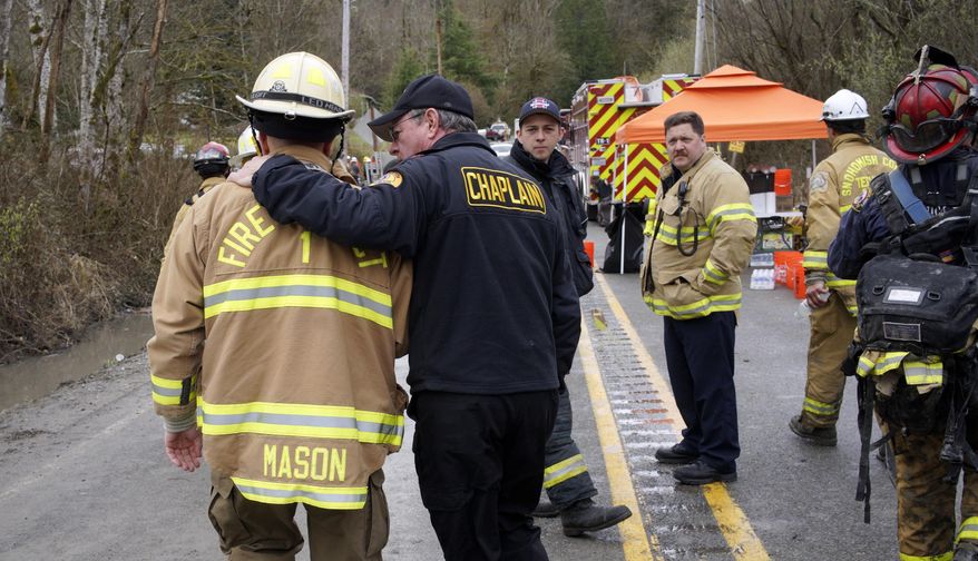 A chaplain from the Washington State Patrol, right, walks with his arm around Snohomish County battalion chief Steve Mason near the scene of a deadly mudslide, Wednesday, March 26, 2014, in Oso, Wash. Sixteen bodies have been recovered, but authorities believe at least 24 people were killed. And scores of others are still unaccounted for, although many of those names were believed to be duplicates or people who escaped safely. (AP Photo/Rick Wilking, Pool)