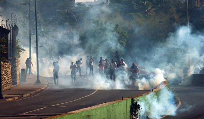 Demonstrators take cover form clouds of tear gas fired by the Bolivarian National Police during an anti-government protest in Caracas, Venezuela, Thursday, March 20, 2014. Thursday dawned with two more opposition politicians, San Cristobal Mayor Daniel Ceballos and San Diego Mayor Enzo Scarano, behind bars. Police used tear gas and water cannons to disperse a student-called protest of several thousand people in Caracas, some of those demonstrating against the arrests of the mayors. (AP Photo/Fernando Llano)