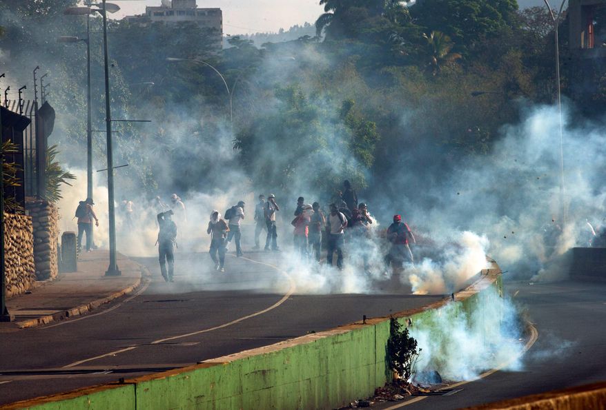 Demonstrators take cover form clouds of tear gas fired by the Bolivarian National Police during an anti-government protest in Caracas, Venezuela, Thursday, March 20, 2014. Thursday dawned with two more opposition politicians, San Cristobal Mayor Daniel Ceballos and San Diego Mayor Enzo Scarano, behind bars. Police used tear gas and water cannons to disperse a student-called protest of several thousand people in Caracas, some of those demonstrating against the arrests of the mayors. (AP Photo/Fernando Llano)