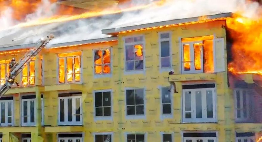 In this image taken from video provided by Karen Jones, a worker lowers himself from a fifth floor balcony before swinging down to the one below as firefighters battle a five-alarm fire at a construction site Tuesday, March 25, 2014, in Houston. The cellphone video, shot by Karen Jones from her nearby office, shows the dramatic rescue of the worker from the burning apartment complex that was under construction. (AP Photo/Karen Jones) NO SALES