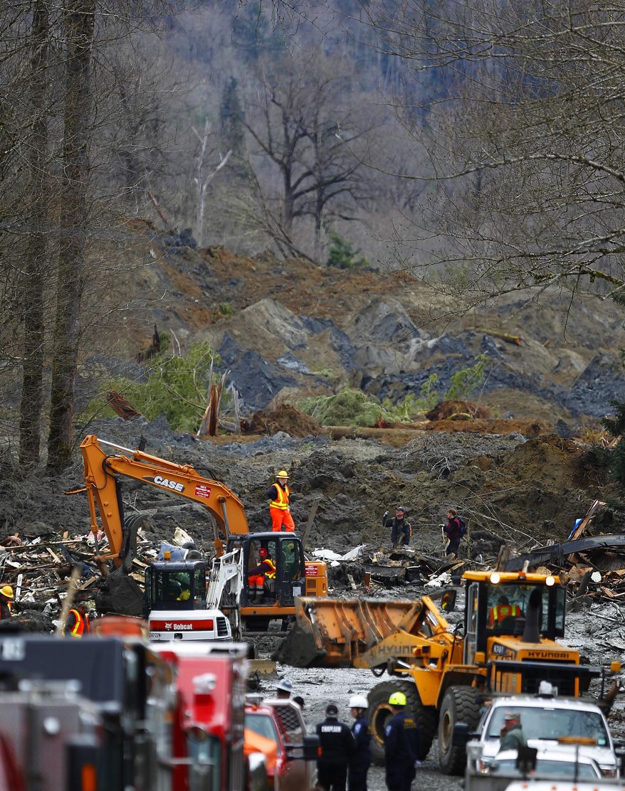 Heavy equipment moves debris on the western edge of the mudslide where it covers Highway 530 Wednesday morning, March 26, 2014, east of Oso, Wash. Washington authorities on Wednesday reduced to 90 the number of people missing from the community wiped out by the mudslide. (AP Photo/The Herald, Mark Mulligan)