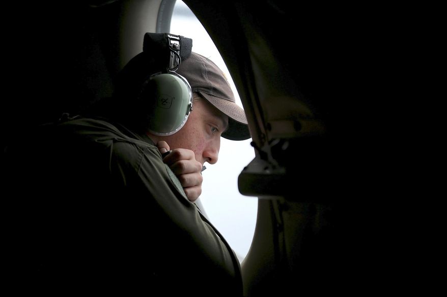 In this Wednesday, March 26, 2014 photo, a crew member on board a Royal Australian Air Force AP-3C Orion, searches for the missing Malaysia Airlines Flight 370 in the southern Indian Ocean. A French satellite scanning the Indian Ocean for remnants of the missing jetliner found a possible plane debris field containing 122 objects, a top Malaysian official said Wednesday, calling it "the most credible lead that we have." (AP Photo/Paul Kane, Pool)
