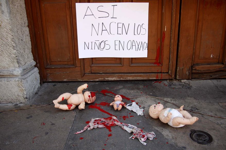 In this Tuesday, Feb. 18, 2014 photo, baby dolls representing children born in the streets are shown during a protest outside the Ministry of Health in Oaxaca , Mexico. The sign on the door reads in Spanish, "The children in Oaxaca are born like this". Women's rights advocates sought international help Thursday in trying to end what they call a pattern of poor indigenous Mexican women being turned away from hospitals while in labor, forcing them to give birth on lawns, patios or parking lots. (AP Photo/Luis Alberto Cruz)