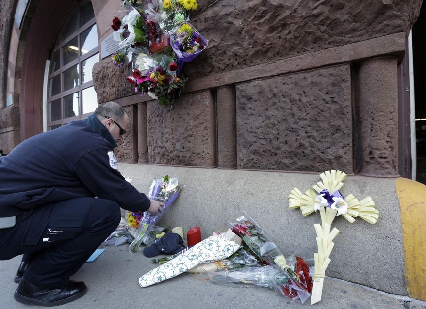 Emergency medical technician David Stewart places flowers at a makeshift memorial on the front of fire station Engine 33/Ladder 15, Thursday, March 27, 2014, in Boston. Engine 33/Ladder 15 was the station of fallen firefighters Lt. Edward Walsh and Michael Kennedy, who lost their lives fighting a nine-alarm blaze in a four-story brownstone in Boston's Back Bay neighborhood Wednesday, March 26, 2014. (AP Photo/Steven Senne)