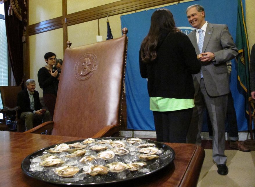 A plate of Olympia oysters sits on a conference table as Gov. Jay Inslee stands nearby after signing a bill making the shellfish the official oyster of Washington state, on Friday, March 28, 2014, in Olympia, Wash. The oysters are small and flat and found in low tide areas, mudflats and gravel bars in estuaries and bays. (AP Photo/Rachel La Corte)