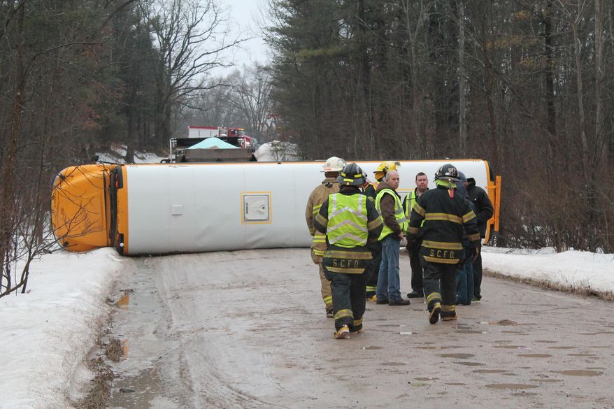 Firefighters respond to the scene after a Greenville Public Schools bus tipped onto its side this morning after losing control on an icy gravel road in Fairplain Township, Mich., on Friday, March 28, 2014. Police say they believe the driver lost control of the bus, which came to rest on its side blocking the entire road. No other vehicles were involved. Greenville school officials say 15-20 students were on the bus at the time, and about a dozen were evaluated at hospitals. Police say students were treated at the scene for minor injuries and five were admitted to a hospital for further treatment. (AP Photo/Daily News, Curtis Wildfong)