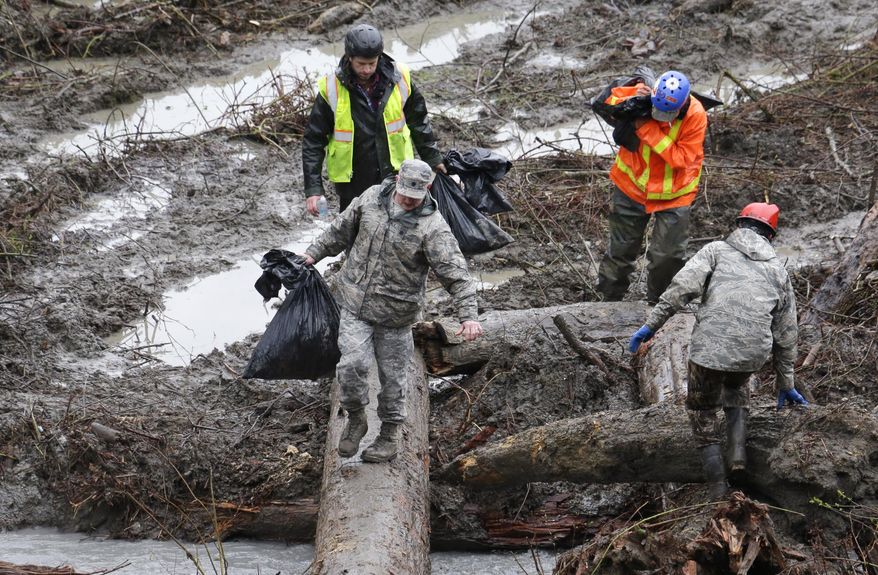 Searchers carry bags of personal belongings collected at the scene of a deadly mudslide Saturday, March 29, 2014, in Oso, Wash. Besides the more than two dozen bodies already found, many more people could be buried in the debris pile left from the mudslide one week ago. Ninety people are listed as missing. (AP Photo/Elaine Thompson, Pool)