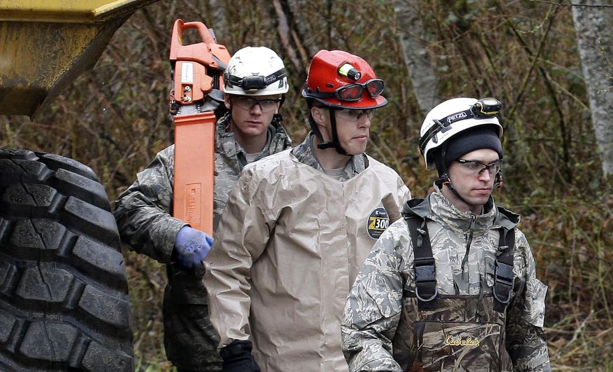 Searchers walk past heavy equipment as they leave the scene of a deadly mudslide, Saturday, March 29, 2014, in Oso, Wash. Besides the more than two dozen bodies already found, many more people could be buried in the debris pile left from the mudslide one week ago. Ninety people are listed as missing. (AP Photo/Elaine Thompson, Pool)