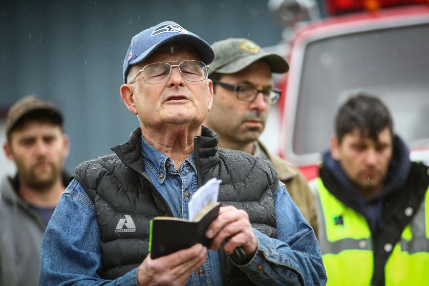 Rev. Michael De Luca offers a prayer before rescue workers and volunteers pause during a state-wide moment of silence to honor the victims of the Oso mud slide in front of the Darrington, Wash., on Saturday, March 29, 2014. Gov. Jay Inslee had asked people across Washington to pause at 10:37 a.m. The huge slide that destroyed a neighborhood in Oso north of Seattle struck at that time on March 22. Authorities say they've found at least 25 bodies and scores remain missing. (AP Photo/seattlepi.com, Joshua Trujillo)