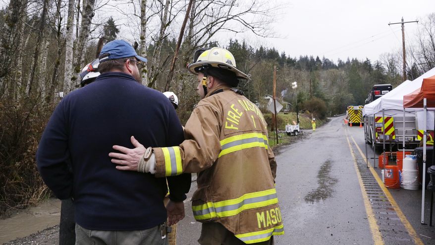 Snohomish County Fire Dept. Battalion Chief Steve Mason, right, briefly greets workers at the scene of a deadly mudslide Saturday, March 29, 2014, in Oso, Wash. Besides the more than two dozen bodies already found, many more people could be buried in the debris pile left from the mudslide one week ago. Ninety people are listed as missing. (AP Photo/Elaine Thompson, Pool)