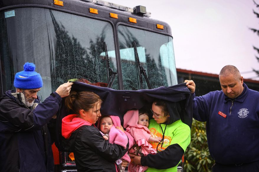 Volunteer Ralph Jones, left, and Tim Perciful of the Mountainview, Black Diamond Fire Department, help keep Klarissa Calviste and her daughter Kielie Braaten, left, and Brooke Odenius and her daughter Bexli dry as they observe a state-wide moment of silence to honor the victims of the Oso mud slide in front of the Darrington, Wash. Fire Department on Saturday, March 29, 2014. Gov. Jay Inslee had asked people across Washington to pause at 10:37 a.m. The huge slide that destroyed a neighborhood in Oso north of Seattle struck at that time on March 22. Authorities say they've found at least 25 bodies and scores remain missing. (AP Photo/seattlepi.com, Joshua Trujillo)
