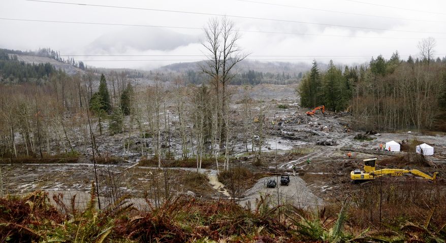A now-barren hillside stands at left overlooking a valley now filled with mud and debris at the scene of a deadly mudslide Saturday, March 29, 2014, in Oso, Wash. Besides the more than two dozen bodies already found, many more people could be buried in the debris pile left from the mudslide one week ago. Ninety people are listed as missing. (AP Photo/Elaine Thompson, Pool)