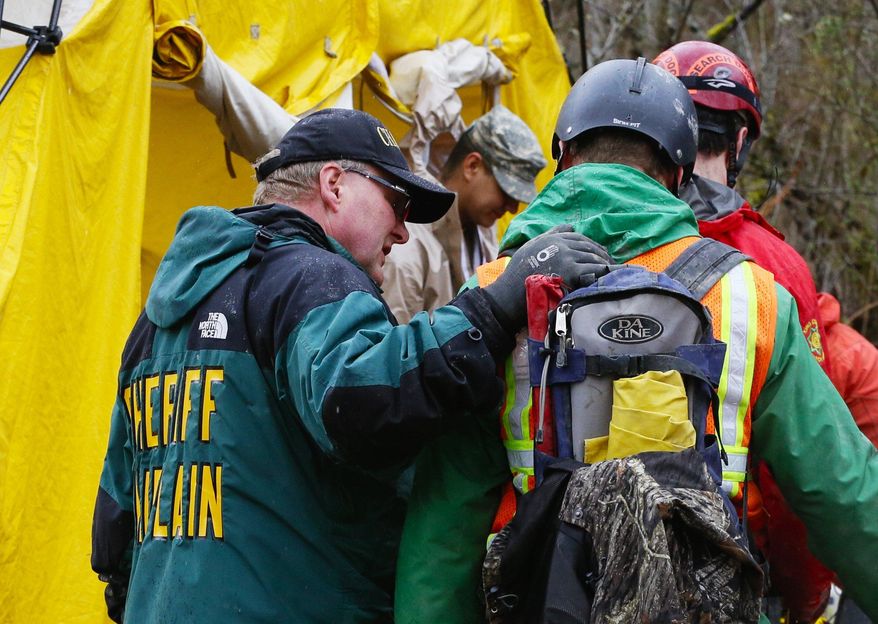 A sheriff chaplain offers a few words to a rescue worker as he enters the decontamination tent area at the west side of the mudslide on Highway 530 near mile marker 37 in Arlington, Wash., on Sunday, March 30, 2014. Periods of rain and wind have hampered efforts the past two days, with some rain showers continuing today. Last night, the confirmed fatalities list was updated to 18, with the number of those missing falling from 90 to 30. (AP Photo/Rick Wilking, Pool)