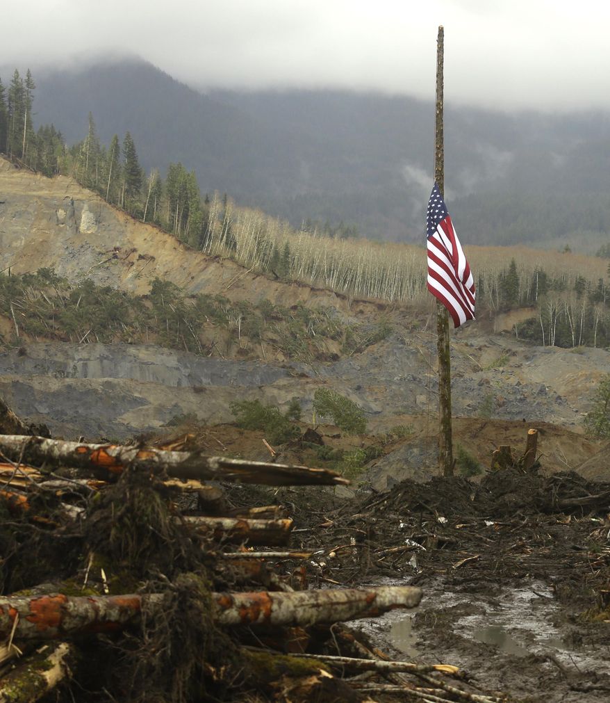 ALTERNATE CROP - A flag flies at half-staff on a log Sunday, March 30, 2014, with the slope of the massive mudslide that struck Saturday, March 22, 2014 in the background. The search for victims of the deadly slide continued Sunday, with crews searching both with heavy machinery and by hand. (AP Photo/Ted S. Warren)