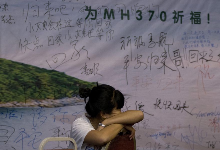 A woman, one of the relatives of Chinese passengers aboard the missing Malaysia Airlines flight MH370 takes a nap on a chair in front of a poster with writings for wishes for the passengers onboard the missing plane at a hotel in Beijing Sunday, March 30, 2014. Several dozen Chinese relatives of passengers on Flight 370 demanded Sunday that Malaysia apologize for its handling of the search for the missing plane and for the prime minister's statement saying it crashed into the southern Indian Ocean. (AP Photo/Andy Wong)