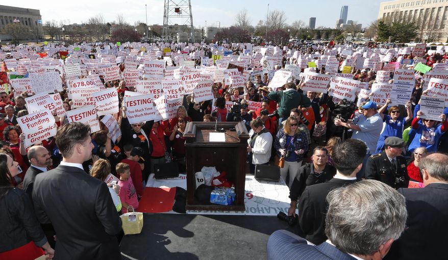 Peter Markes, left, 2014 Oklahoma Teacher of the Year, watches from the stage as a huge crowd of teachers, parents and children amass at the Oklahoma Capitol building in Oklahoma City, Monday, March 31, 2014, to call for an increase in school funding, which hasn't reached its pre-recession levels despite the addition of tens of thousands more students to the state's classrooms. (AP Photo/Sue Ogrocki)