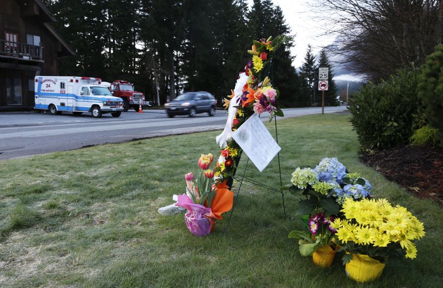 A car passes a small flower memorial, Monday, March 31, 2014, at the fire station in Darrington, Wash., at the beginning of another week of searching for victims of the massive mudslide that hit the nearby community of Oso,Wash. Crews have cleared a path through the muck and devastation wrought by Washington's deadly mudslide, making the painstaking search for victims easier. The makeshift road completed over the weekend links one side of the 300-acre debris field to the other. (AP Photo/Ted S. Warren)
