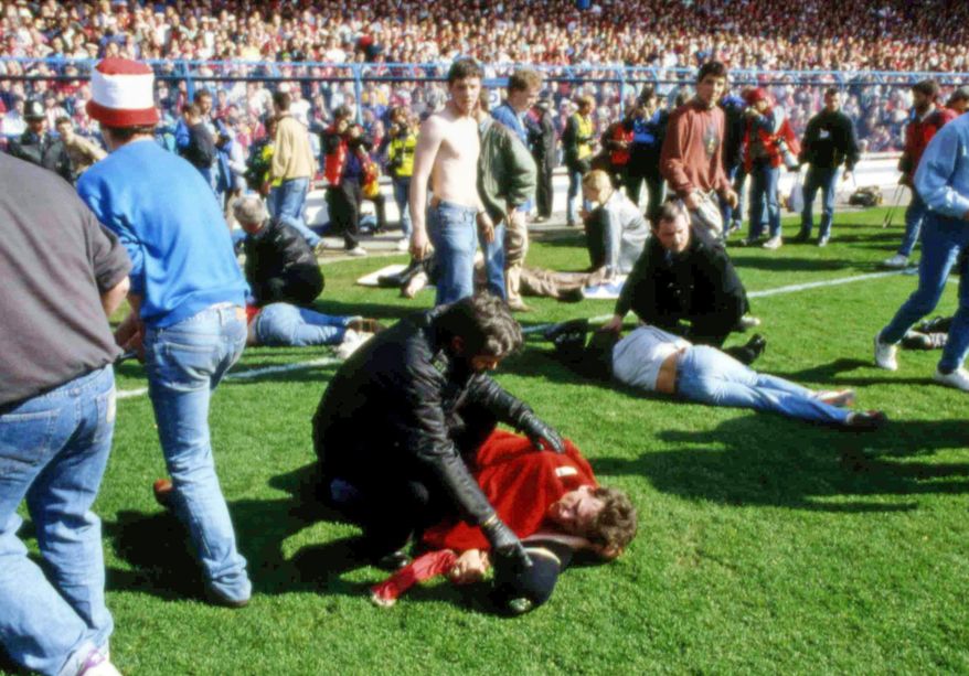 FILE- In this file photo dated April 15, 1989, police, stewards and supporters care for supporters on the field after many fans were crushed onto the barriers at Hillsborough Football Stadium, in Sheffield, England, on April 15, 1989, when fans surged forward during the Cup semi-final between Liverpool and Nottingham Forest at Hillsborough Stadium killing 96 people. After years of campaigning to expose alleged wrongdoing by the authorities, new inquests into Britain’s worst sports disaster are beginning Monday March 31, 2014, with the families of the 96 Liverpool fans crushed to death at Hillsborough seeking verdicts of unlawful killing. (AP Photo, FILE)
