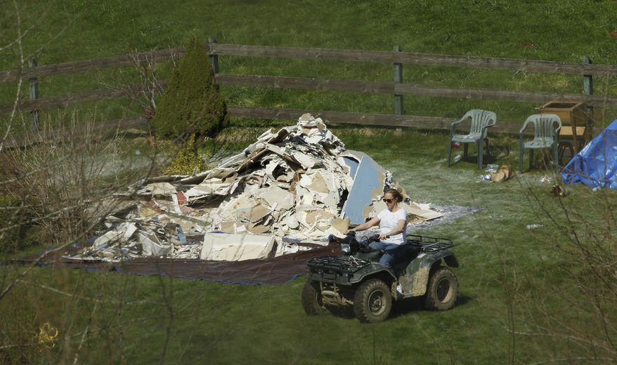 A woman rides an all-terrain vehicle past a pile of drywall removed from the home of Don and Elaine Young, Tuesday, April 1, 2014, near Darrington, Wash., very near the site of the deadly mudslide that hit the community of Oso,Wash. on March 22, 2014. The home was damaged by floodwaters after the slide backed up the Stillaguamish River. (AP Photo/Ted S. Warren)