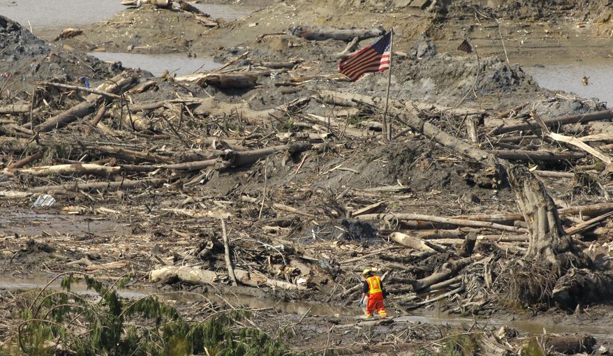 A searcher walks through a channel of water as a flag flies in the debris field Monday, March 31, 2014, near Darrington, Wash., at the site of the massive mudslide that hit the nearby community of Oso,Wash. on March 22, 2014. (AP Photo/Ted S. Warren)