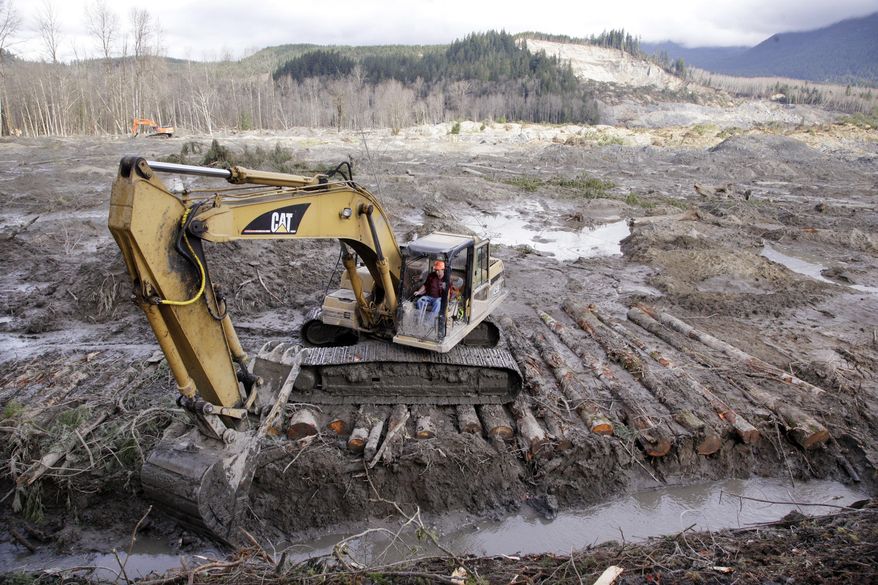 An excavator clears a drainage channel at the scene of a deadly mudslide, torn loose from the hillside at upper right, Wednesday, April 2, 2014, in Oso, Wash. The March 22 mudslide has killed at least 29 and another 13 are unaccounted for. (AP Photo/Elaine Thompson)