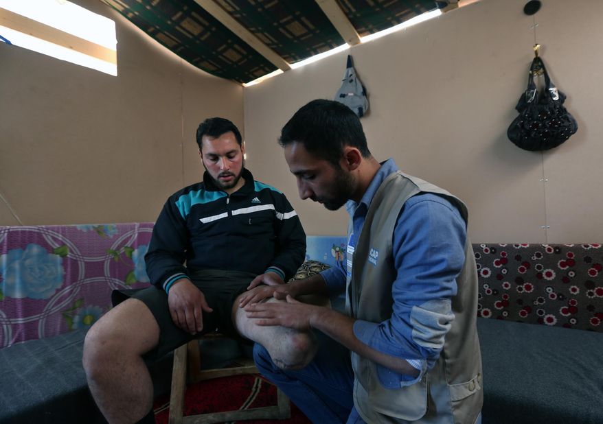 In this Thursday, March 27, 2014 photo, Ziad Zehori, 24, left, who lost his leg in a Syrian government airstrike on Sept. 25, 2013, sits as Mohammed Kurdi, right, a physiotherapist for Handicap International, checks his thigh, at the Syrian refugee camp in Zahleh, in the Bekaa valley, Lebanon. Syria’s civil war, which entered its fourth year last month, has killed more than 140,000 people. An often overlooked figure is the number of wounded more than 500,000, according to the International Committee of the Red Cross. An untold number of those, there’s no reliable estimate even, have suffered traumatic injuries that have left them physically handicapped. (AP Photo/Bilal Hussein)