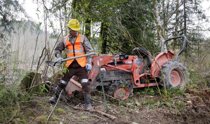 A searcher makes his way past a tractor that landed at the edge of the debris field after being tossed about in a deadly mudslide, Wednesday, April 2, 2014, in Oso, Wash. Officials have so far confirmed the deaths of 29 people, although only 22 have been officially identified in information released Wednesday morning by the Snohomish County medical examiner's office. (AP Photo/Elaine Thompson)