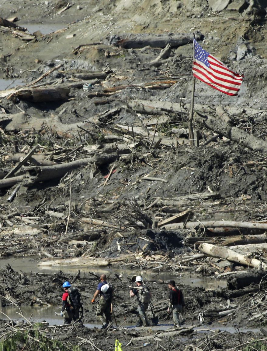 Workers carrying hand tools and shovels walk past a U.S. flag, Tuesday, April 1, 2014, near Darrington, Wash., in the debris field of the deadly mudslide that hit the community of Oso,Wash. on March 22, 2014. (AP Photo/Ted S. Warren)