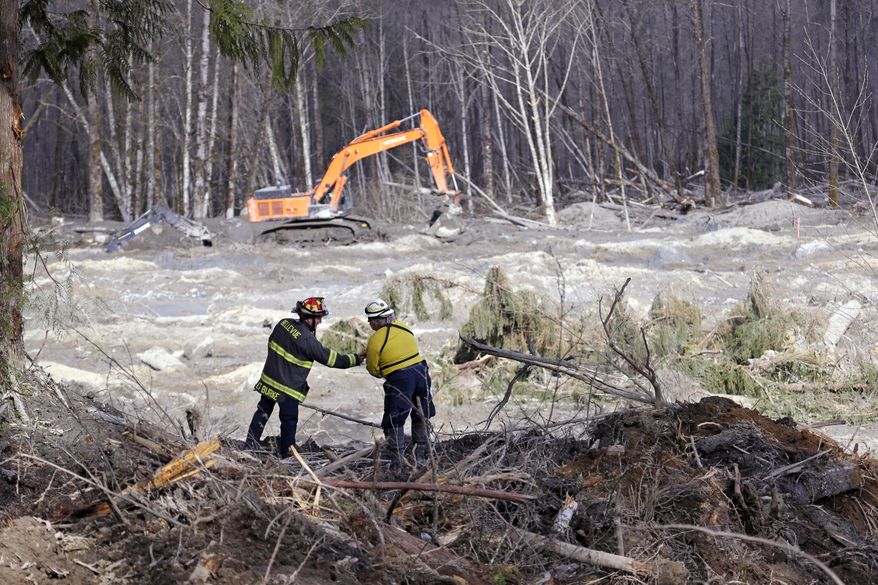 Bellevue, Wash., Fire Dept. Lt. Richard Burke, left, reaches across to shake hands with Benton County assistant fire chief Jack Coats as the two overlook the scene of a deadly mudslide Wednesday, April 2, 2014, in Oso, Wash. Officials have so far confirmed the deaths of 29 people, although only 22 have been officially identified in information released Wednesday morning by the Snohomish County medical examiner's office. (AP Photo/Elaine Thompson)
