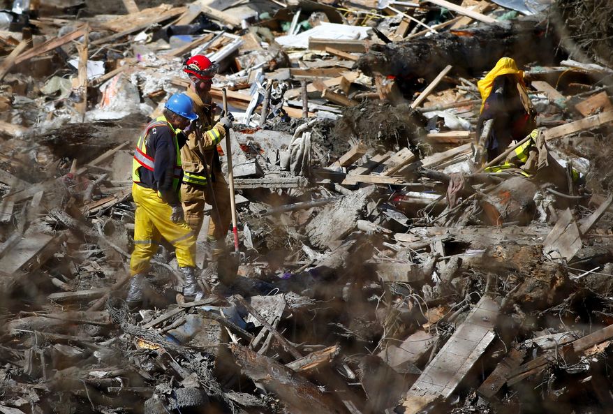 Two workers look down at the expansive field of twisted wires, broken wood and other mangled debris, seen from an emergency and work access road connecting Arlington to Darrington at the west site of the mudslide on Highway 530, near Oso, Wash., on Tuesday, April 1, 2014. The death toll from the March 22 mudslide has increased to 28. (AP Photo/The Seattle Times, Lindsey Wasson) SEATTLE OUT; USA TODAY OUT; MAGS OUT; TELEVISION OUT; NO SALES; MANDATORY CREDIT TO BOTH THE SEATTLE TIMES AND THE PHOTOGRAPHER