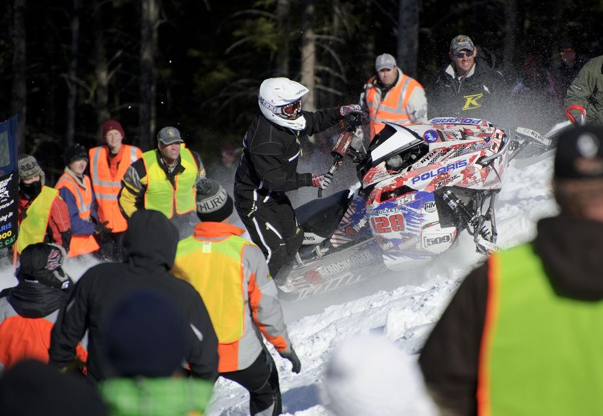In this photo taken on March 22, 2014, the hill help surround Tyler Crockett as he finds his way up the course at the World Championship Snowmobile Hill Climb in Jackson Hole,Wyo . The volunteers throw themselves into harms way to save riders and their machines from tumbling down the mountain. (AP Photo/Jackson Hole News & Guide, Price Chambers)