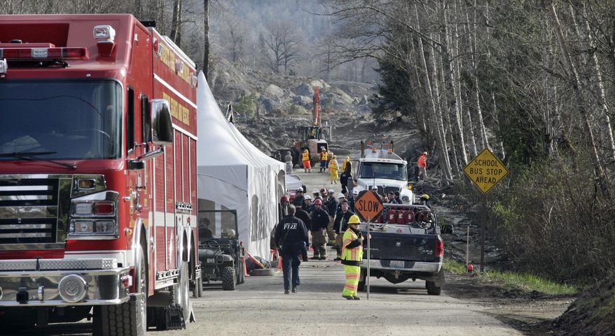 Emergency personnel stage on Highway 530 as work to clear debris from the roadway left behind from a deadly mudslide continues behind, Wednesday, April 2, 2014, in Oso, Wash. Officials have so far confirmed the deaths of 29 people, although only 22 have been officially identified in information released Wednesday morning by the Snohomish County medical examiner's office. (AP Photo/Elaine Thompson)