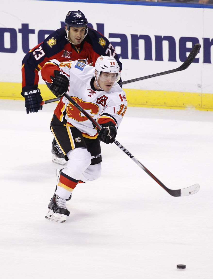 Calgary Flames left wing Mike Cammalleri (13) shoots the puck as Florida Panthers center Scott Gomez (23) follows during the first period of an NHL hockey game in Sunrise, Fla., Friday, April 4, 2014. (AP Photo/Terry Renna)