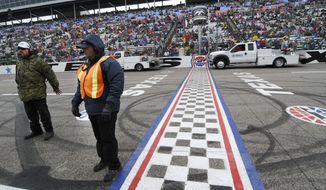 Track security guards Patrick Reyes, left, and Richard Gyure stand by the start-finish line as jet dryers blow dry the strait away before a rain delayed start of the NASCAR Sprint Cup Series auto race at Texas Motor Speedway in Fort Worth, Texas, Sunday, April 6, 2014. (AP Photo/Ralph Lauer)
