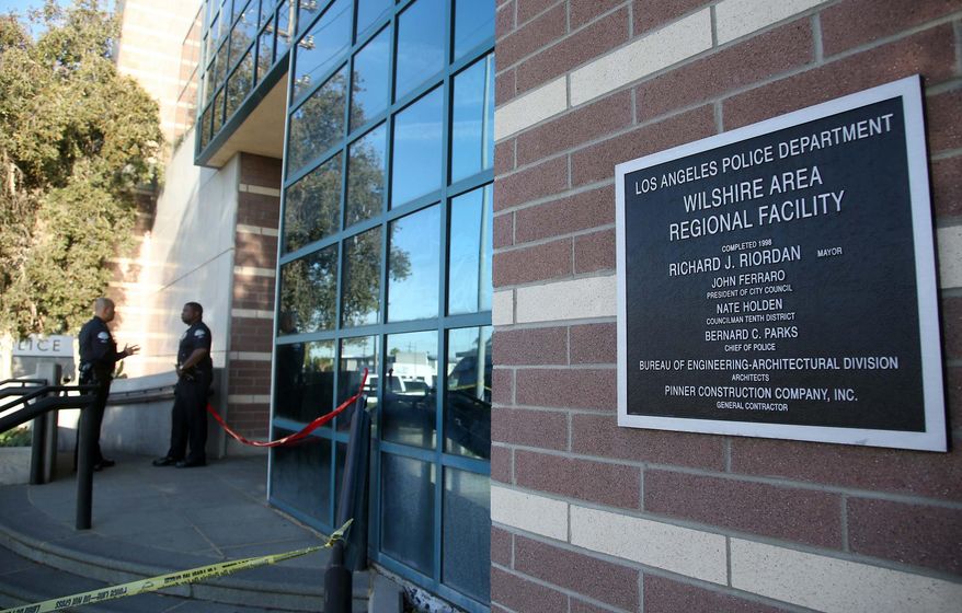 Los Angeles police officers stands outside the West Traffic Division station Tuesday, April 8, 2014, in Los Angeles, after an officer was shot and wounded inside the station Monday evening. A gunman who opened fire inside the police station, hitting one officer several times, was hospitalized early Tuesday in critical condition after he was wounded in the ensuing gunbattle, authorities said. (AP Photo/Nick Ut )