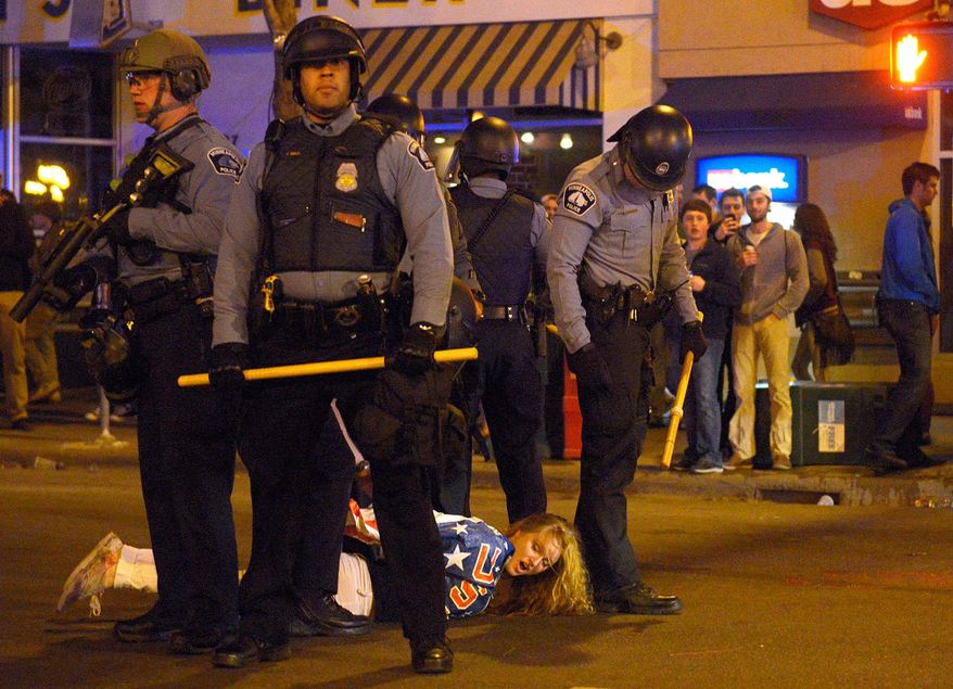 Police stand over a women who was detained during a raucous celebration by University of Minnesota hockey fans that resulted in several arrests Thursday night, April 10, 2014 in Minneapolis. Hundreds of students and other hockey fans took to the streets in Dinkytown near campus to celebrate the Gophers' last-second Frozen Four semifinal win over North Dakota. (AP Photo/The Minnesota Daily, Amanda Snyder)