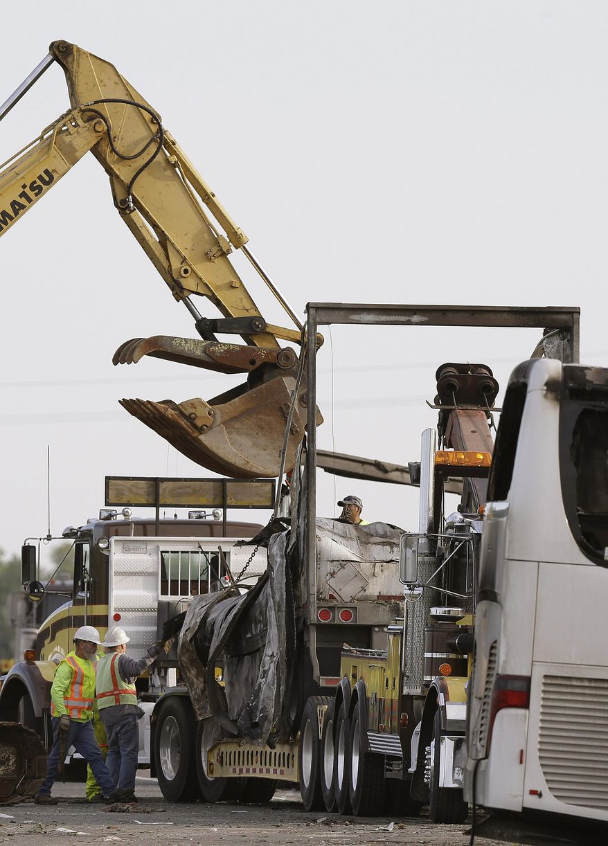 Workers load part of a FedEx truck that crashed into a tour bus on Interstate 5 Thursday onto a tow truck in Orland, Calif., Friday, April 11, 2014. At least ten people were killed and dozens injured in the fiery crash between the truck and a bus carrying high school students on a visit to a Northern California College. (AP Photo/Jeff Chiu)